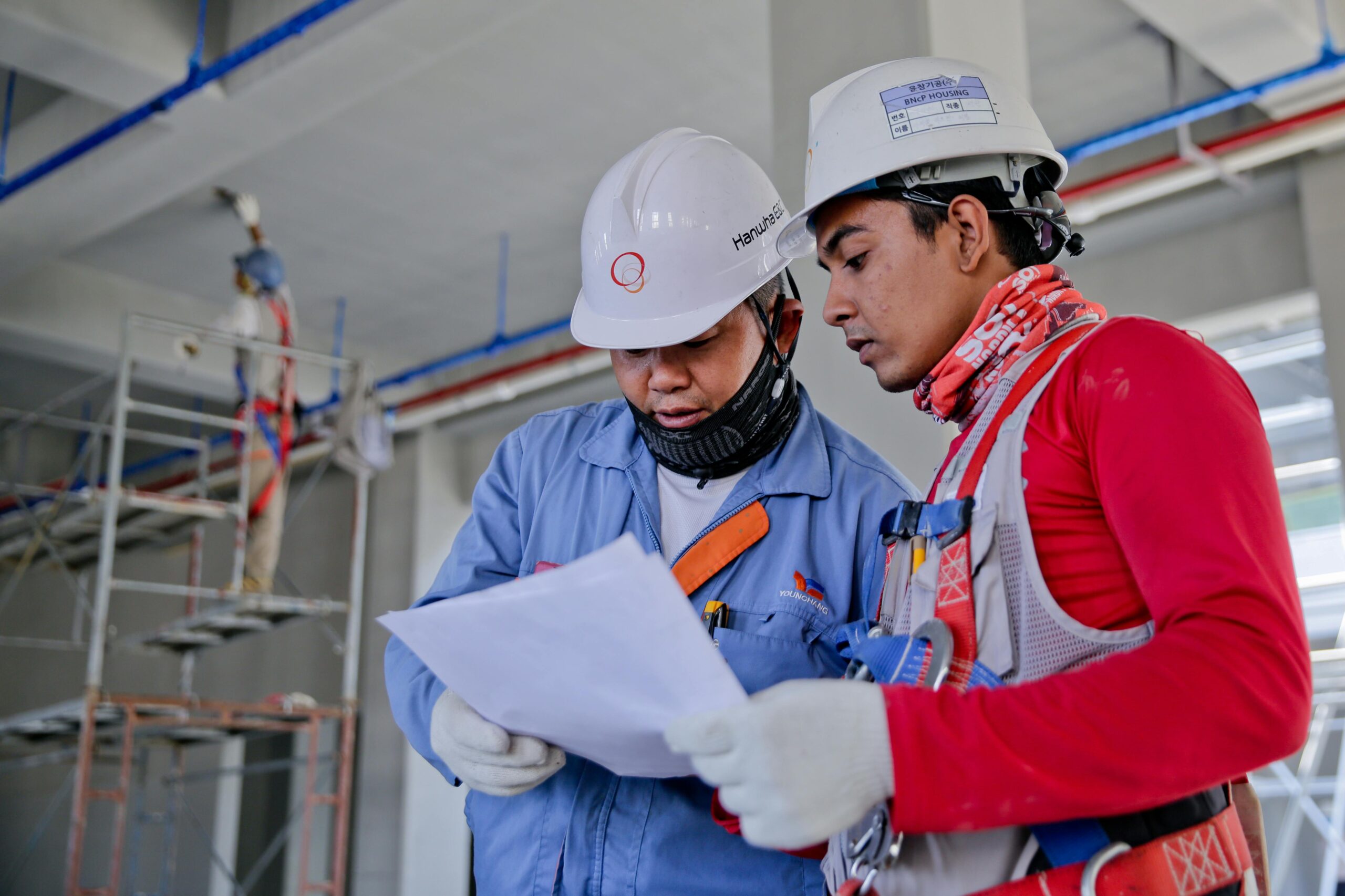 Inicio Two engineers in safety helmets reviewing construction plans at a worksite.