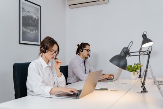 Two call center agents using laptops and headsets in a modern office setting.